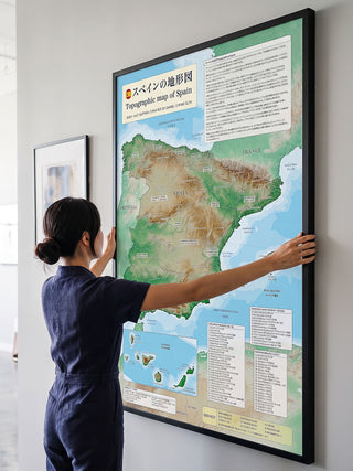白い壁にスペイン地形図のB0大判ポスターを掛けるところ。額装した設置イメージで、額縁は商品に含まれません